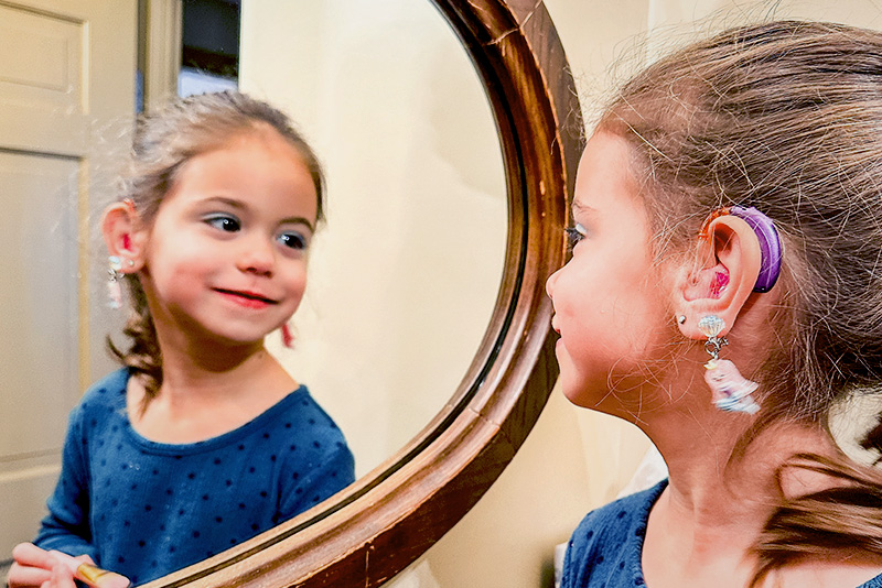 A young girl with hearing aids inserted looks at herself in a mirror