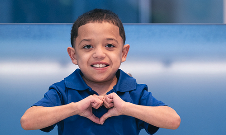 Boy wearing blue shirt holds hands in the shape of a heart