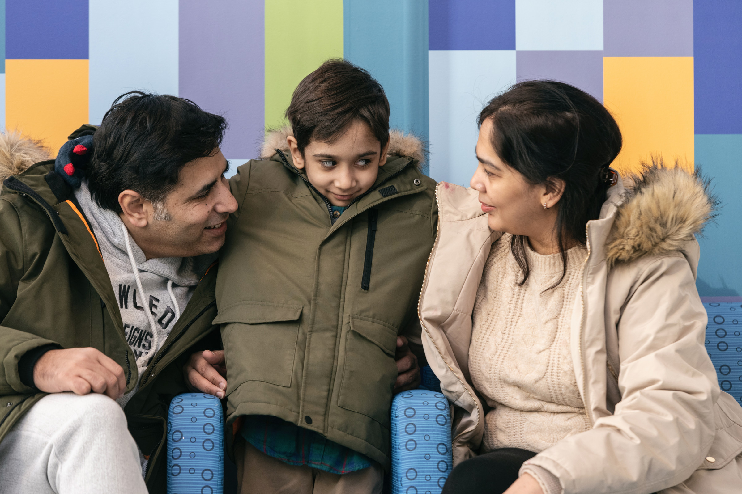 Little boy wearingn winter jacket huddles next to parents in hospital hallway