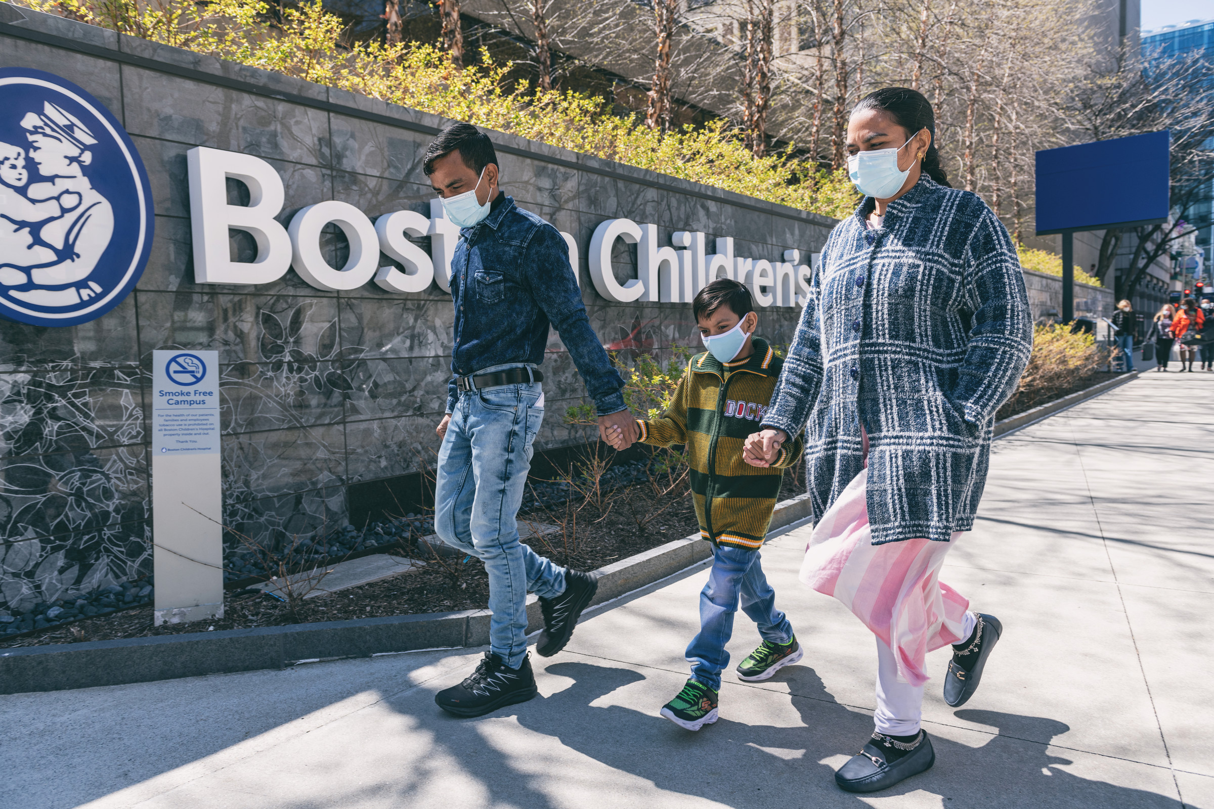 Parents on each side of boy hold his hand as they enter Boston Children's Hospital campus